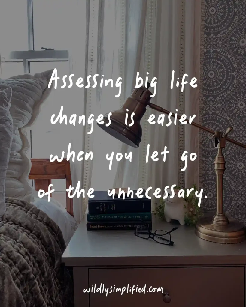 Quote text of "Assessing big life changes is easier when you let go of the unnecessary." overlayed on a dark image of a bedroom nightstand.