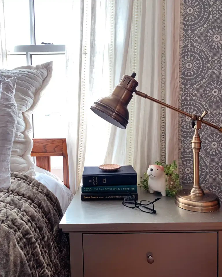 A nightstand sitting beside a bed, clutter free with just a stack of books, ready glasses, lamp, and a plant sitting on top of it