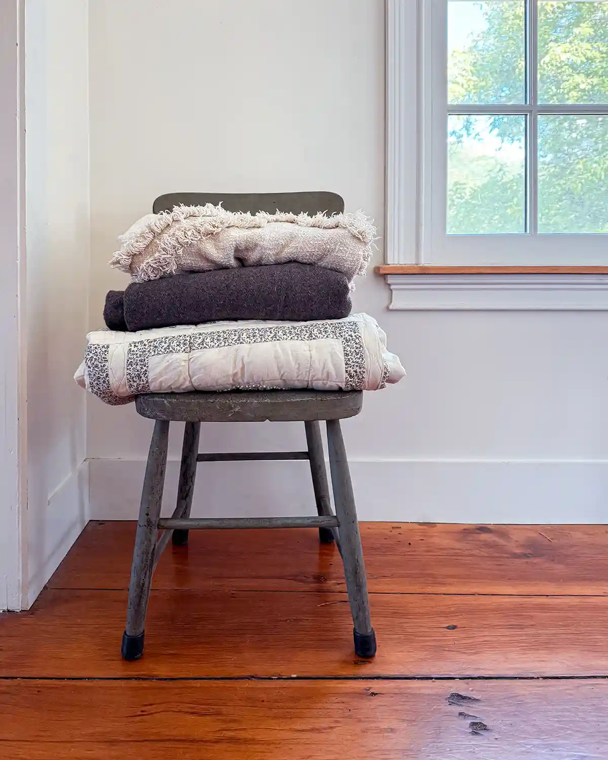 A clutter free nook in a hallway between bedrooms with a stack of textured blankets sitting on a chippy green chair